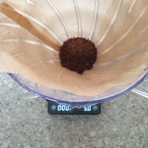 5g을 가르키는 저울 위에 드리퍼가 있고 그 드리퍼 안에는 분쇄된 원두가 있다.