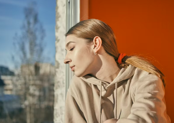 따뜻한 햇살 아래 창가에 앉아 눈을 감고 휴식을 취하는 여성