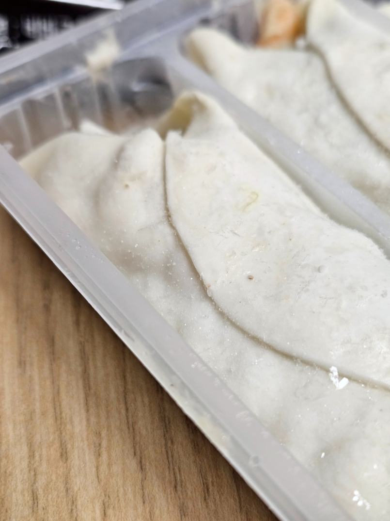 비비고 통새우 만두 개봉 후 트레이에 담긴 냉동 만두 모습으로 반달형 만두가 보이고 만두피가 강조됨