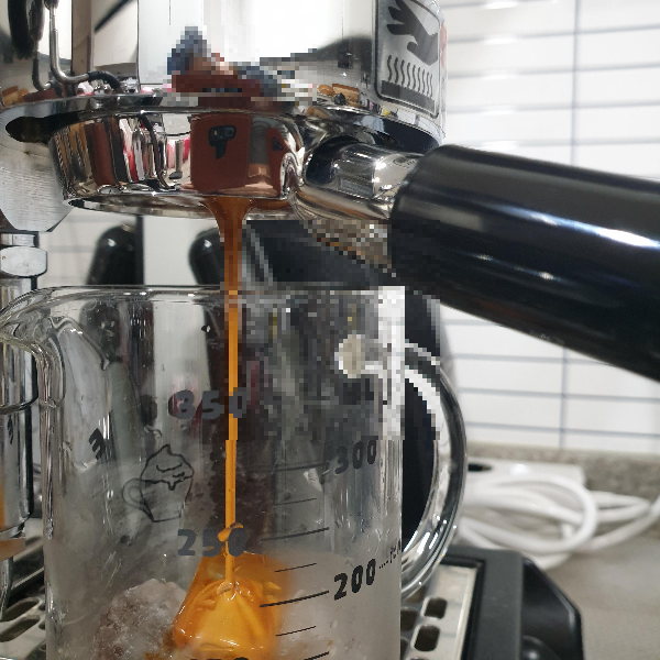 에스프레소 머신에 얼음이 든 컵이 놓여있고 그 컵에 에스프레소가 추출되고 있다.