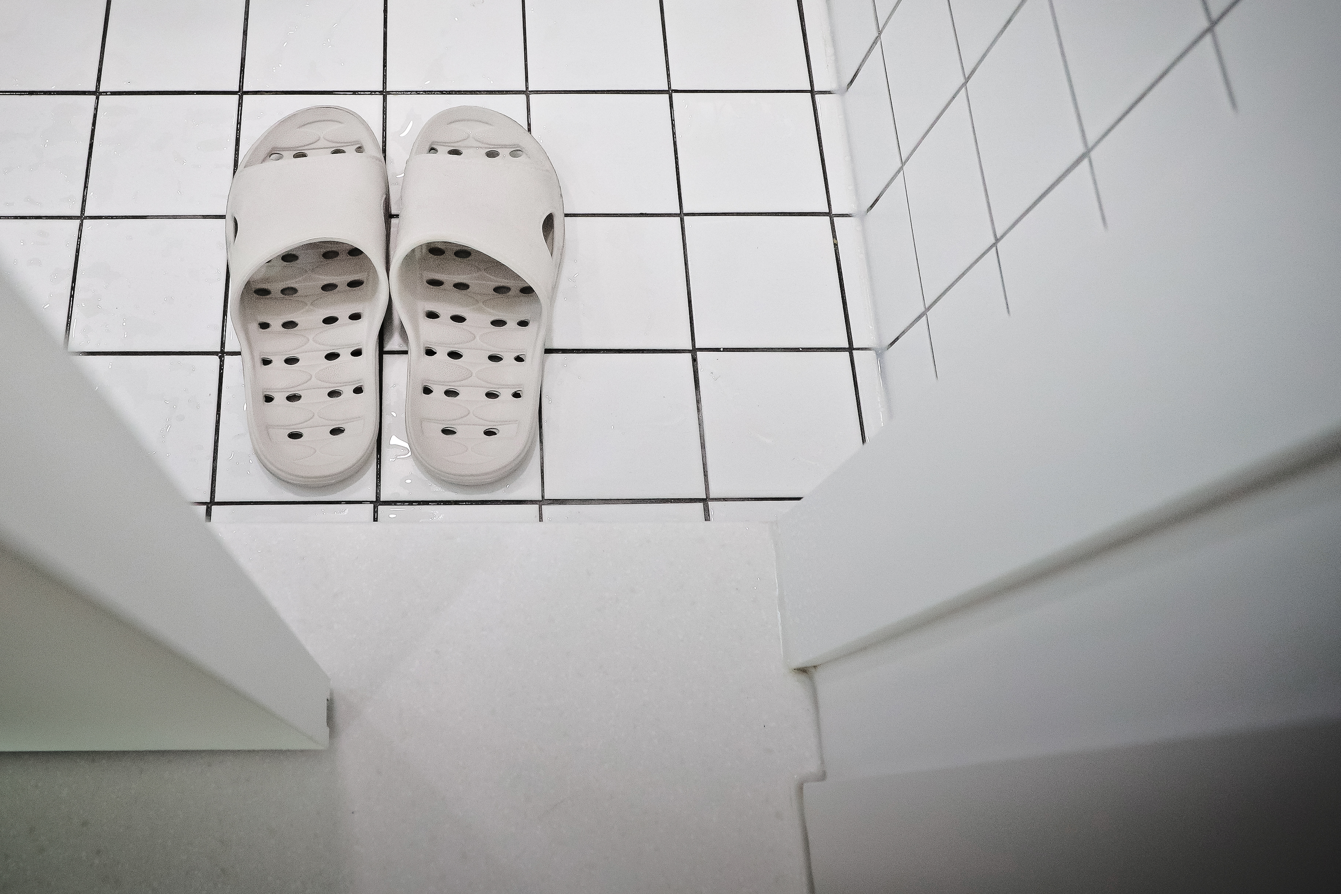 흰색 타일 바닥 위에 놓인 흰색 구멍 뚫린 욕실 슬리퍼 한 켤레
