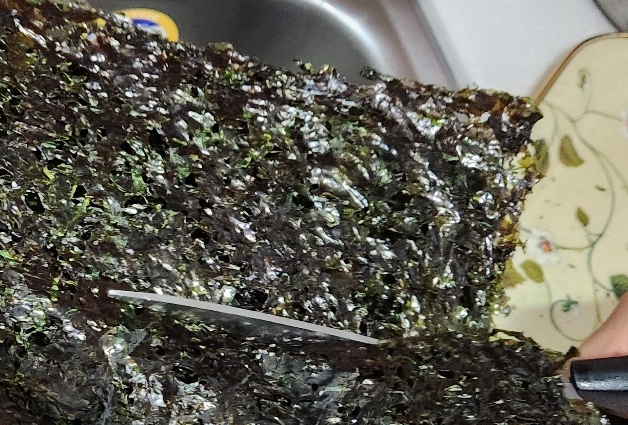 곱창김을 먹을 수 있게 준비하는 과정으로 구운 곱창김을 가위를 사용해 먹을 수 있는 크기로 자르는 사진입니다.