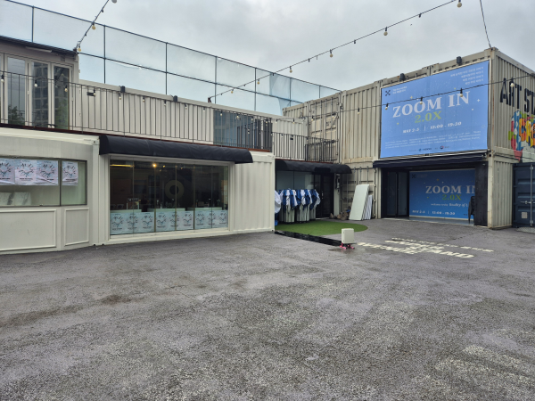 언더스탠드에비뉴 내부 광장, 하얀색 컨테이너 건물들과 'ZOOM IN BOX' 행사 안내 현수막