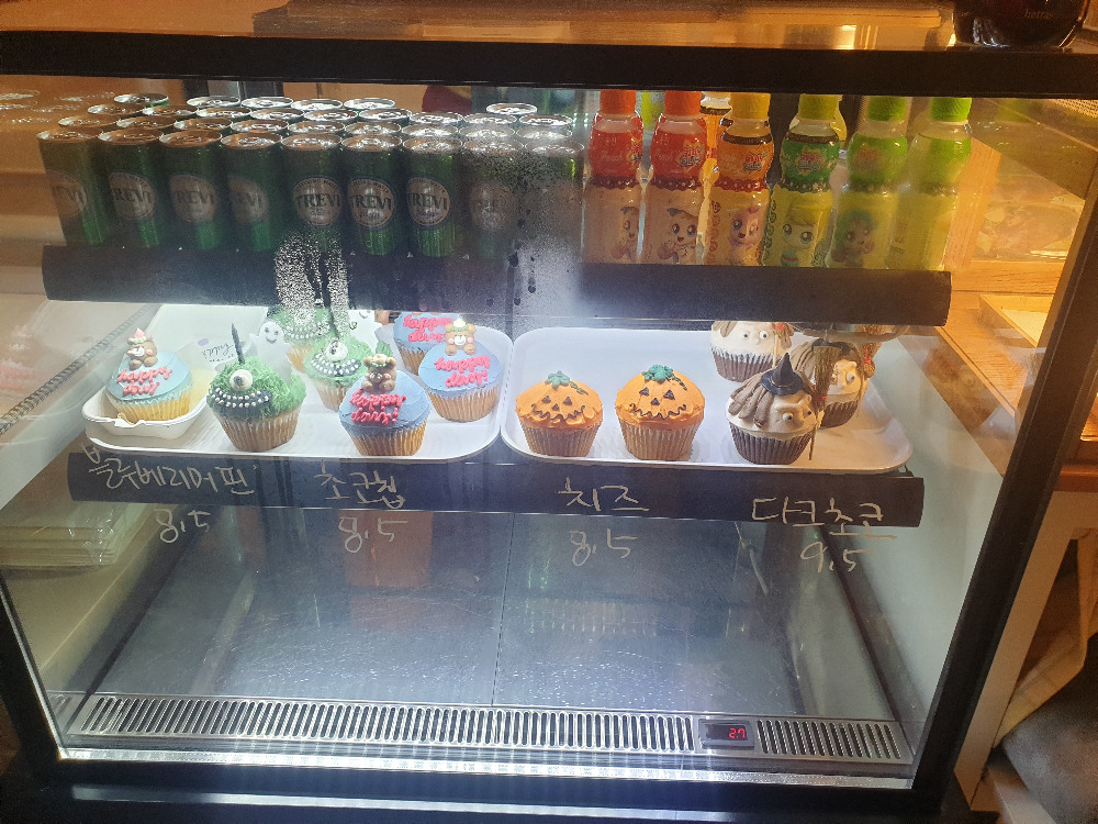 냉장 진열대에 컵케익과 음료가 진열되어 있다. 컵케익은 호박, 마녀, 도깨비 등 할로윈 시즌 한정판이다.