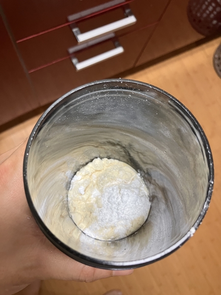 쉐이커 컵 안에 담긴 단백질 보충제 파우더와 그 위에 얹어진 하얀색 뉴트리코스트 크레아틴 가루