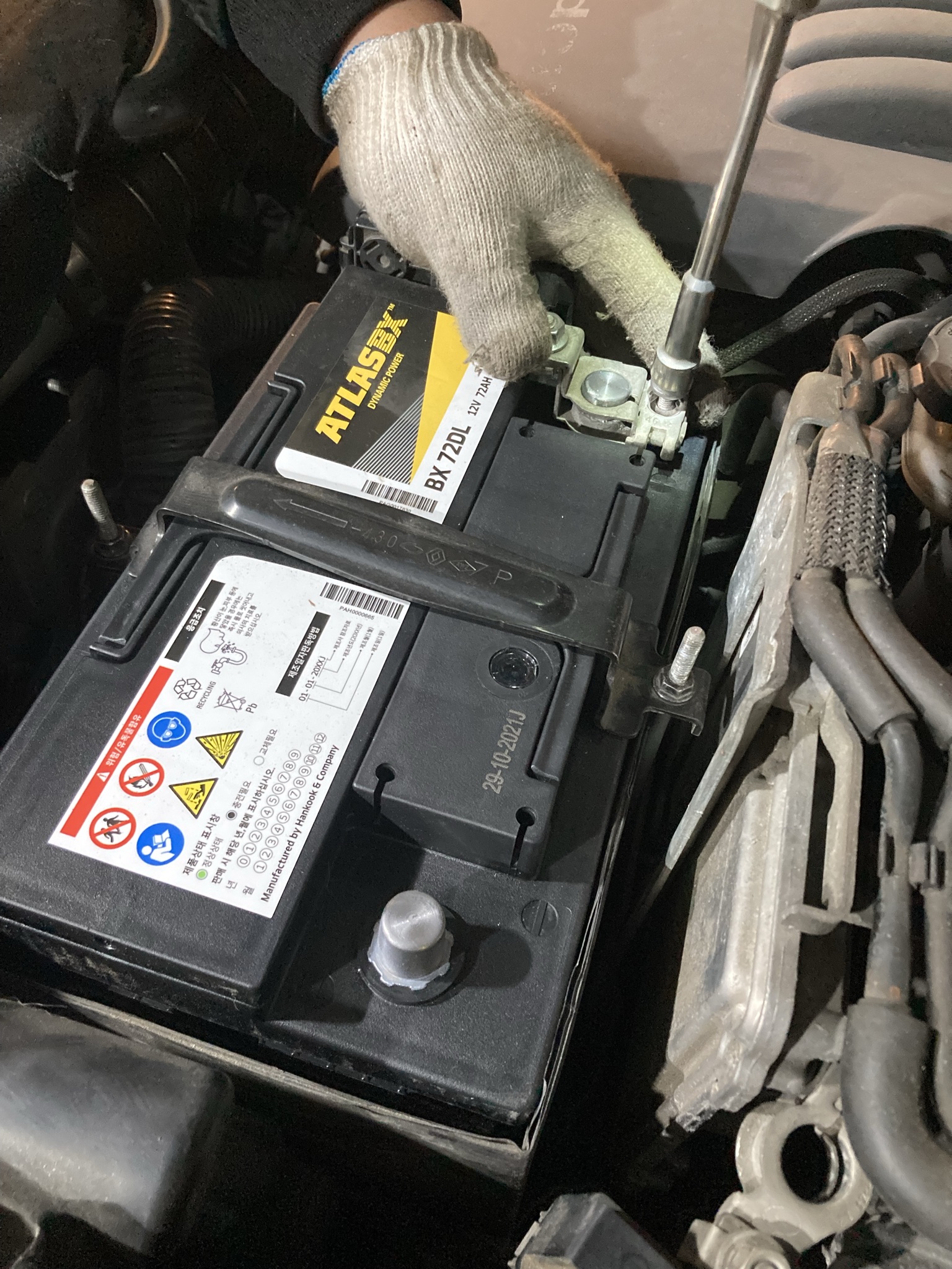 정비사가 장갑을 끼고 엔진룸 안 아트라스 배터리를 고정하는 작업 장면