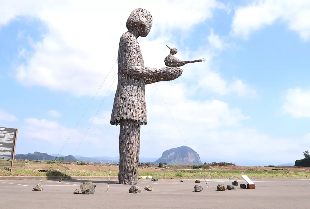 제주 올레길 10코스 섯알오름 정상 부근에 설치된 파랑새 조형물과 그 뒤로 펼쳐진 제주의 평화로운 중산간 풍경.