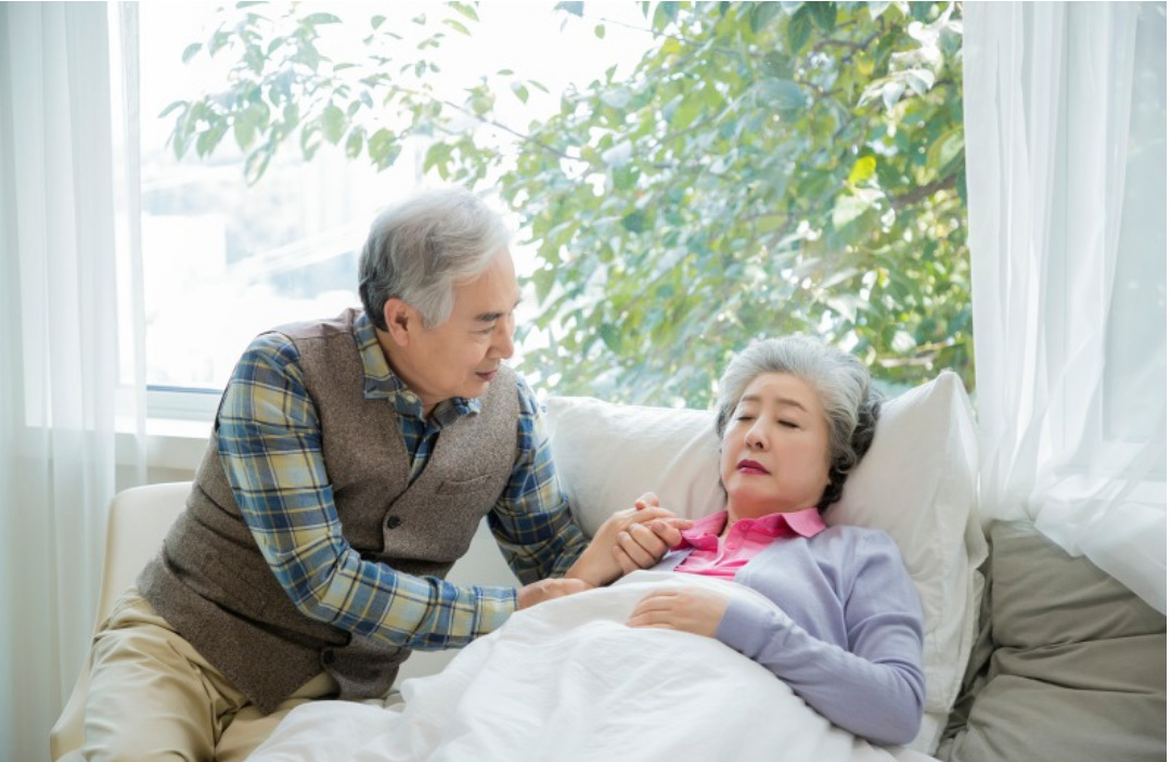 할머니가 침대에 누워있고 할아버지가 간호를 하고 있다.