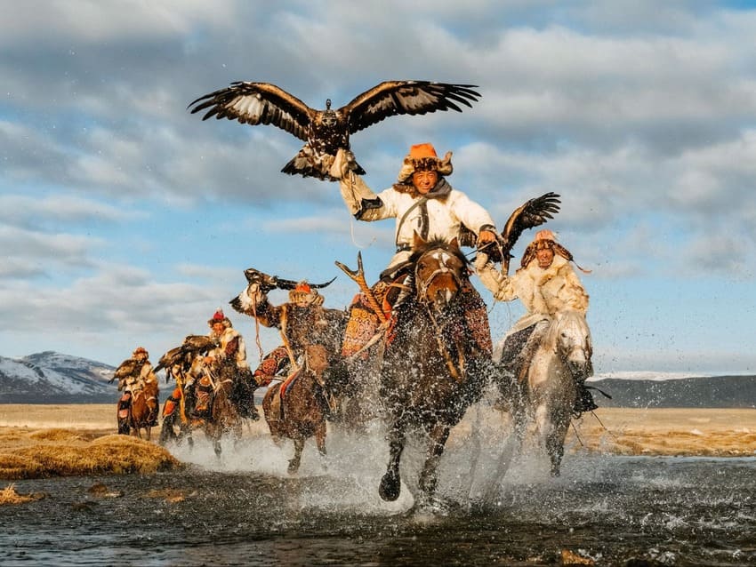 몽골 서부 초원에서 말을 타고 질주하며 독수리를 높이 든 전통 독수리 사냥꾼들