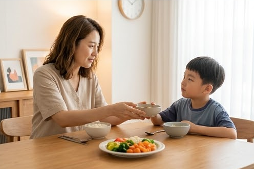 아들에게 작은 그릇을 건네며 미소 짓는 엄마와 채소 접시