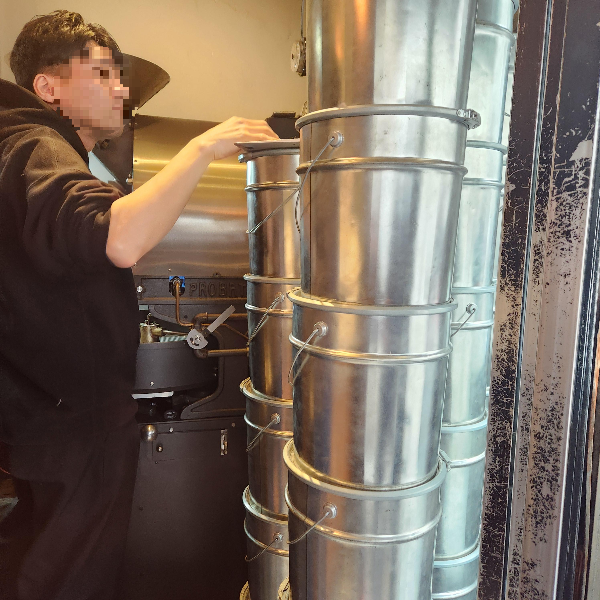 카페 안에 커다란 로스터기가 있다. 사장님이 생두 보관통을 살피고 있다.