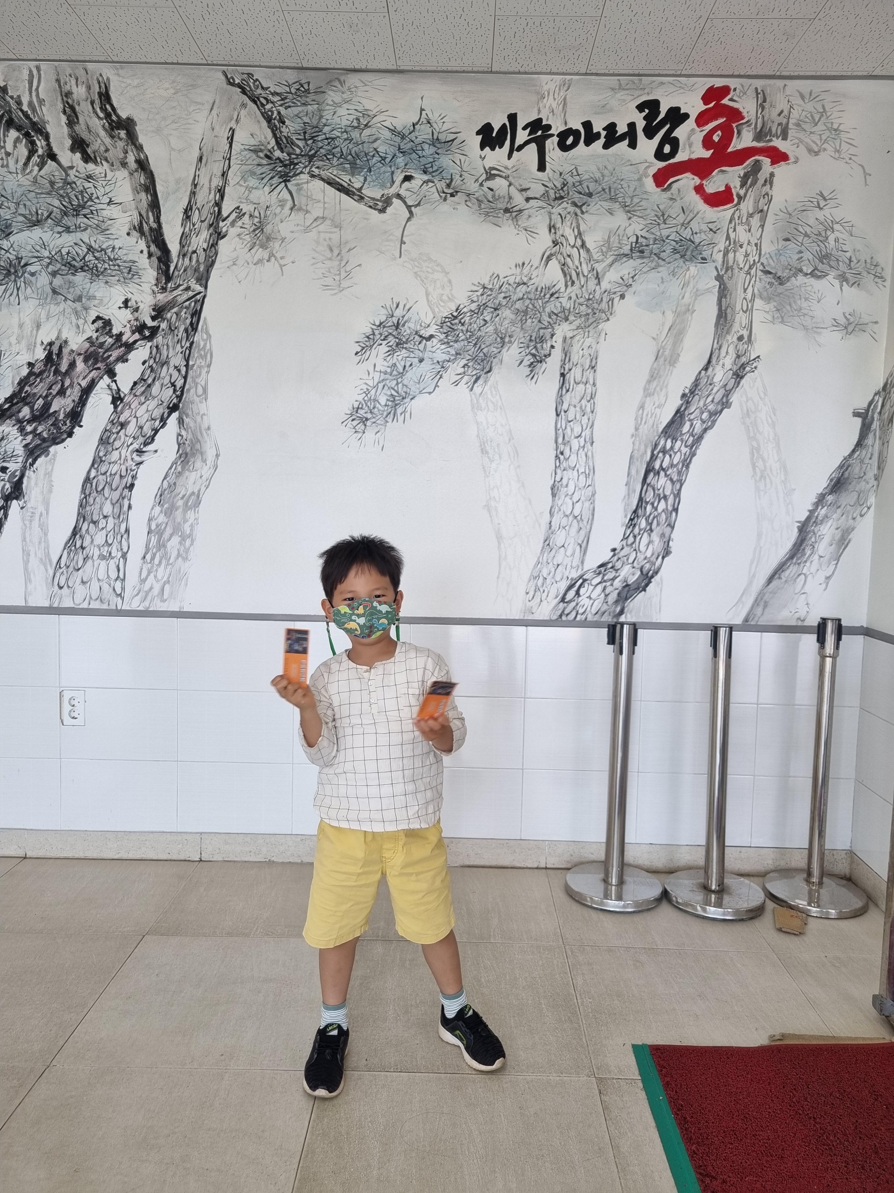 수묵화로 제주아리랑 혼과 소나무가 그려져있도 아이가 티켓을 들고 있다.