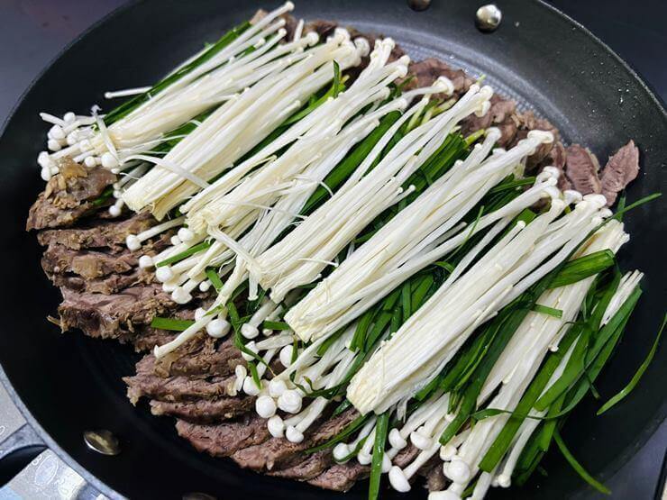 냄비 안에 얇게 썬 아롱사태와 고기 위에 부추와 팽이 버섯이 올려져 있는 사진이다.