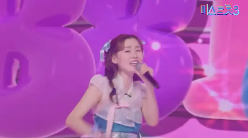 미스트롯3- 보라색 배경 앞 망사 반팔 한복을 입고 왼손으로 마이크를 들고 노래하는 나영