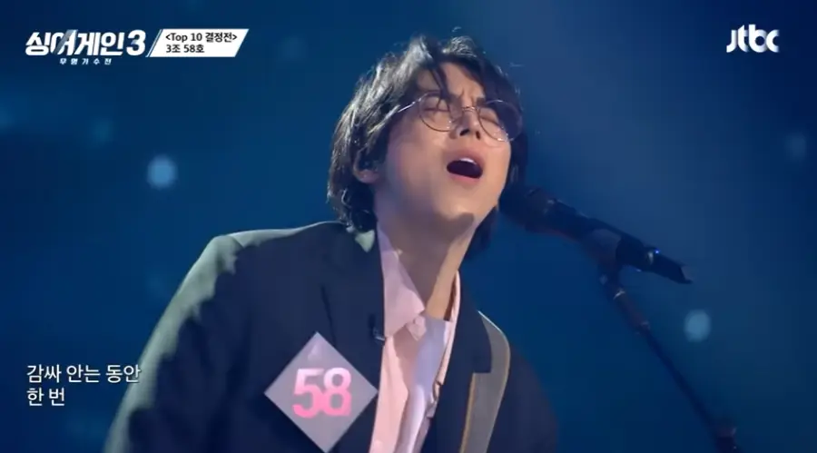 싱어게인3-
검은색 무대배경 웨이브진 머리칼이 얼굴에 자연스레 내려오고 남색 탸켓&#44; 분홍 셔츠 안 흰면티 스탠딩마이크앞에 서서 눈감고 노래하는 58호