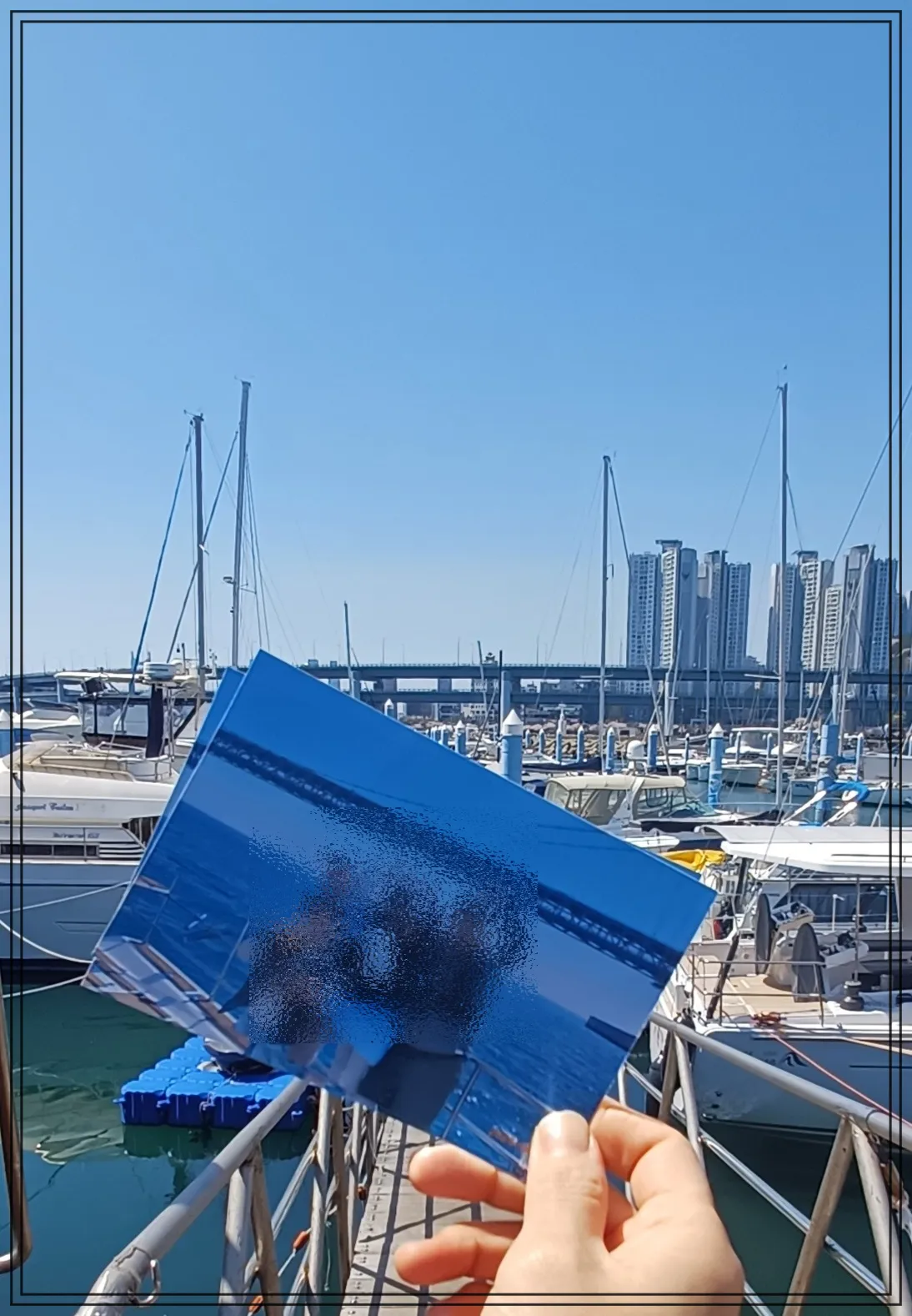 멀리-광안대교보이고-높은-아파트-가깝게-가족끼리-찍은-사진을-들고-있는-손-배경은-요트장