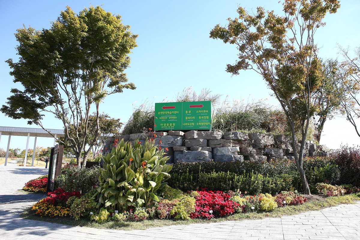 Flower beds and a stone wall with a direction sign beside a paved path at Suncheon Bay National Garden