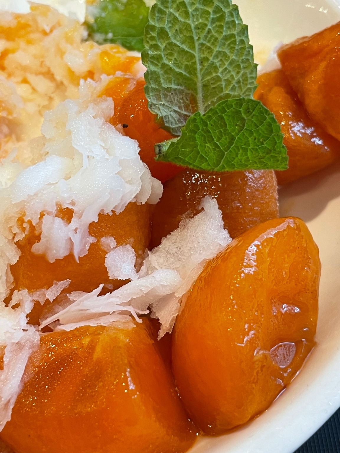 Close-up of frozen ripe persimmon and mint leaves on Korean persimmon bingsu with milk snow ice.
