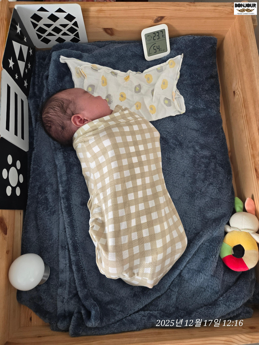 신생아 침대에 아기가 누워있으며, 온도는 23.7도 습도는 54%를 가리키는 이미지