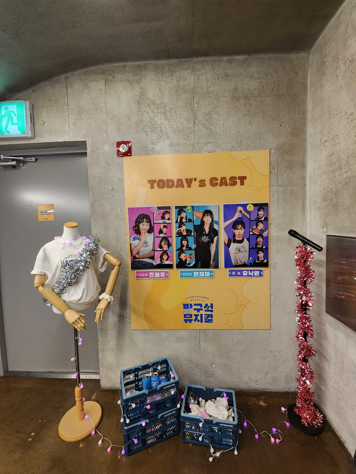 뮤지컬 방구석 뮤지컬 2024년 11월 7일 캐스팅 보드 지금이 - 전혜주 최지현 - 한재아 한 솔 - 유낙원 캐스팅 보드는 벽에 붙어있고 그 앞에 왼쪽부터 오른쪽으로 흰색 반팔티에 반짝이 어깨끈을 왼쪽 어깨부터 오른쪽 옆구리 아래로 쓴 상반신만 있는 마네킹 맥주캔이 든 파란색 박스 3개(알전구로 꾸며진 상태) 제일 오른쪽에 빨간 반짝이로 마이크 대가 돌돌 쌓여진 스탠딩 마이크가 놓여져 있음
