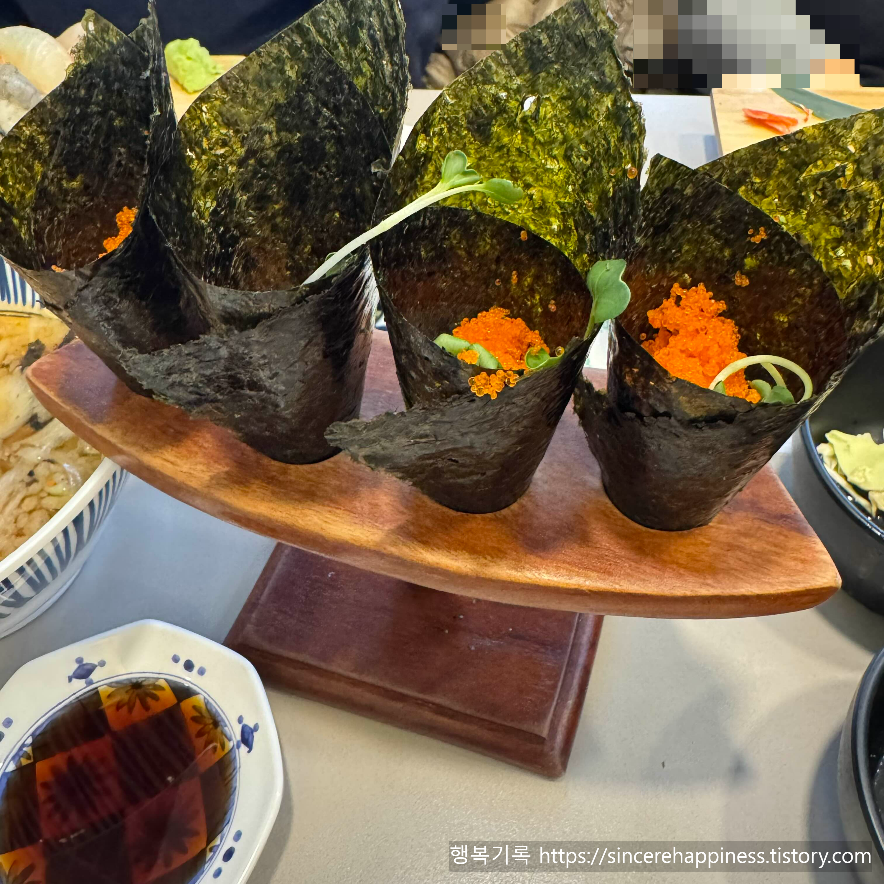 나무 스탠드에 꽂혀 있는 주황색 날치알이 가득 올라간 마끼 4개 모습