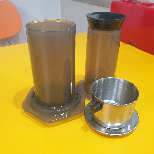 노란 테이블 위에 몸통과 플린저가 분리된 에어로프레스와 베트남 핀이 올려져 있다.