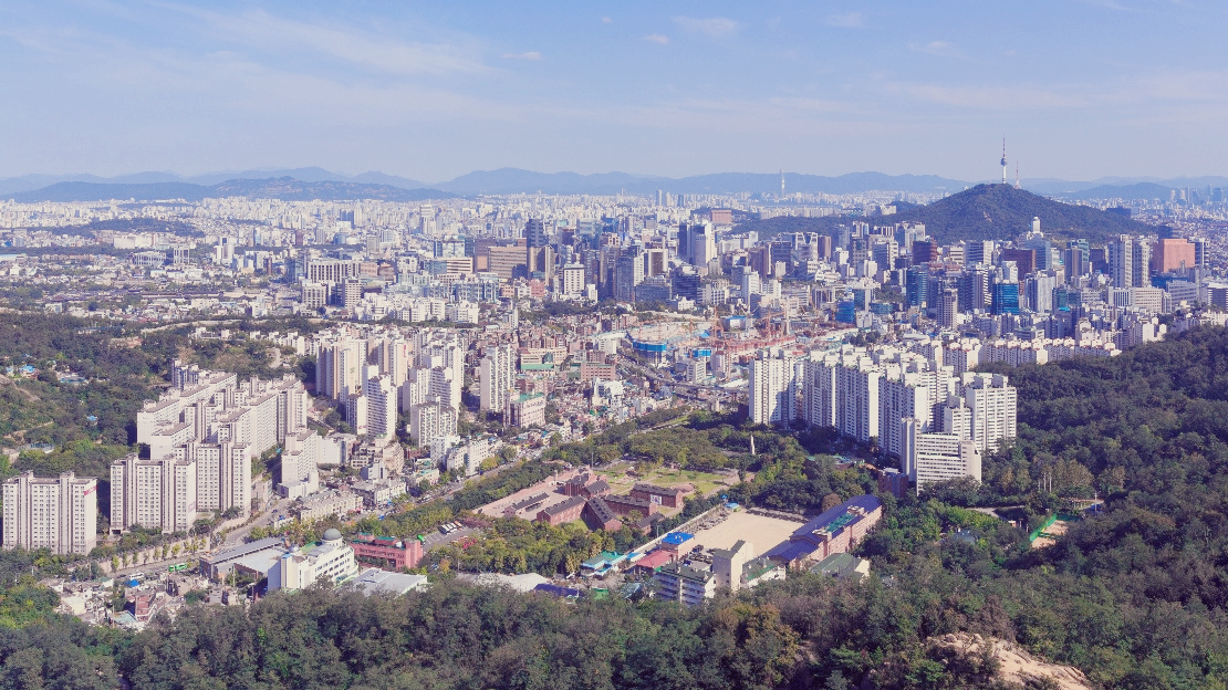 서울 도심의 조감도. 산 능선과 아파트 단지, 고층 빌딩이 혼재된 도시 풍경이며, 멀리 N서울타워가 보인다.