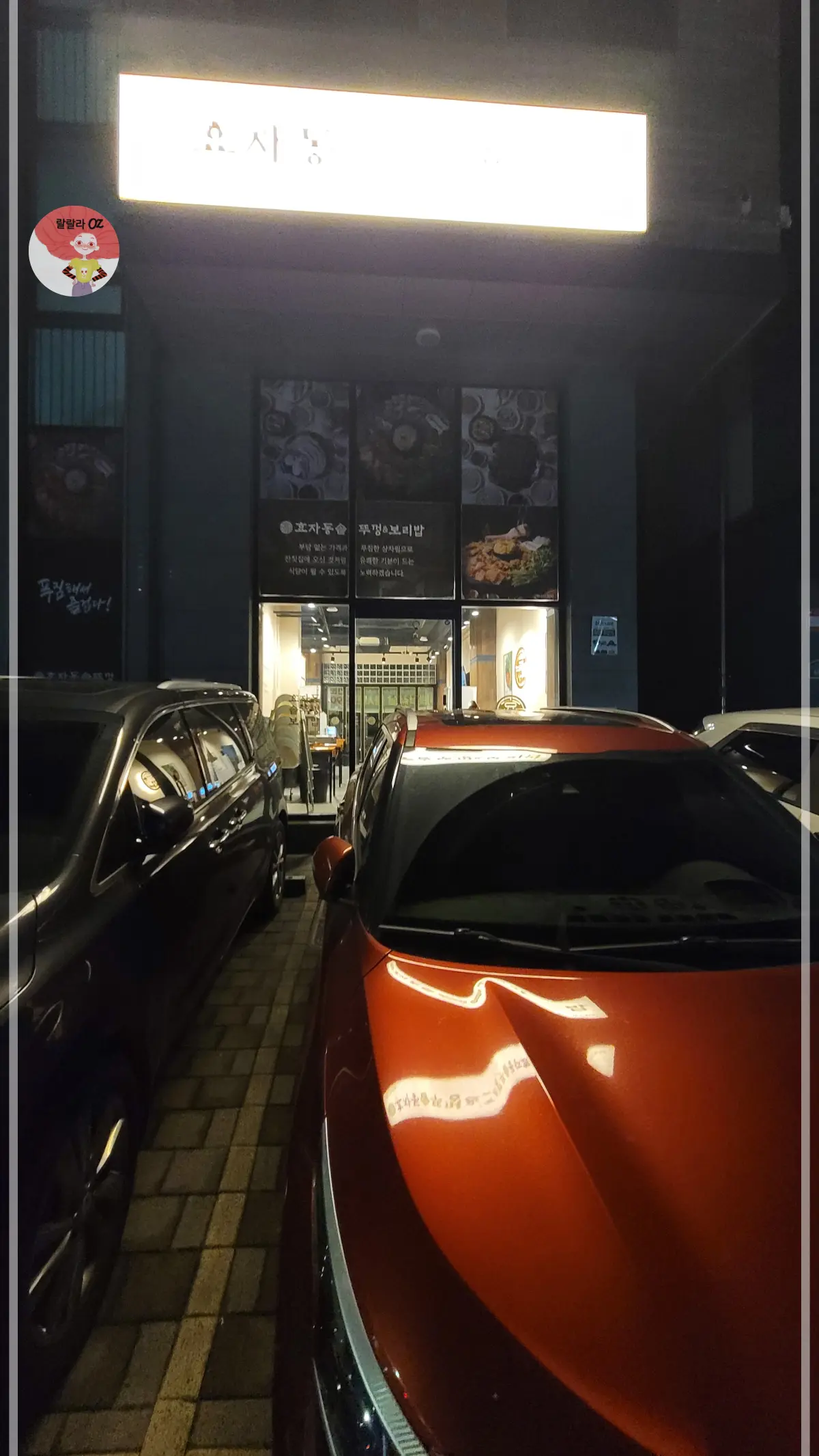 경기-남양주-효자동솥뚜껑-보리밥집-다산점-외관
밤에 음식점 입구가 밝은 간판과 따뜻한 조명으로 환하게 빛나며, 주차된 차량과 내부 좌석이 보이는 아늑한 분위기입니다.