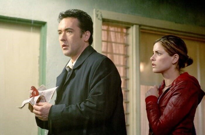 비 오는 밤, 모텔 앞에서 놀란 표정으로 서 있는 남자와 긴장한 듯 옆에 서 있는 여자. 영화 '아이덴티티(Identity)'의 한 장면.