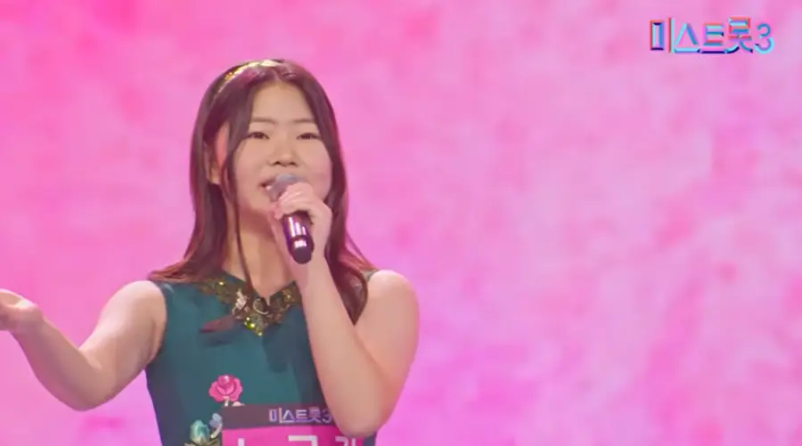 미스트롯3-
초록색 민소매 옷을 입고 어깨까지 오는 머리에 금색 머리띠를 하고 왼손으로 마이크를 잡고 오른손은 먼곳을 가리키며 노래하는 노규리