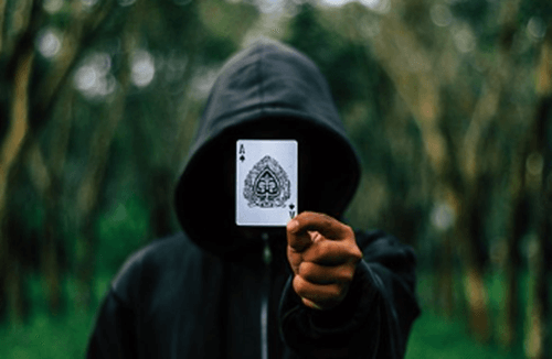 숲에서 후드가 달린 옷을 입고 있으며 머리가 보이지 않게 쓰고 에이스 카드를 들고 있는 모습니다.