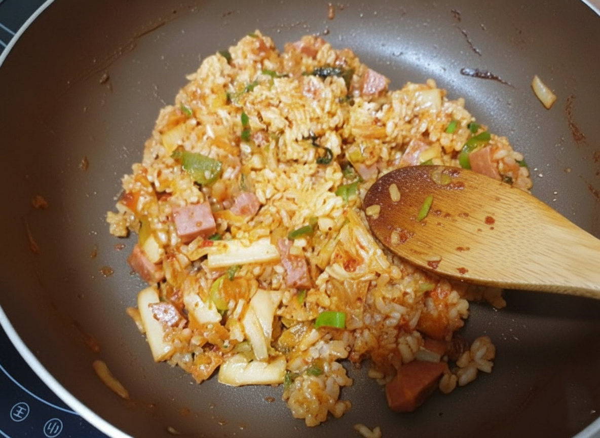 인덕션 위에 놓인 갈색 프라이팬에서 스팸과 김치, 대파를 함께 볶고 있는 모습