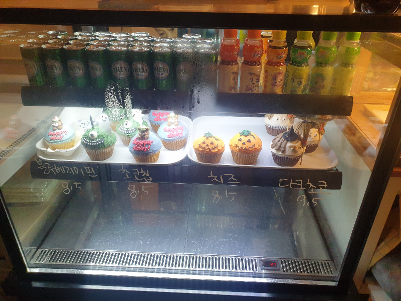 냉장 진열대에 컵케익들과 음료가 놓여 있다.