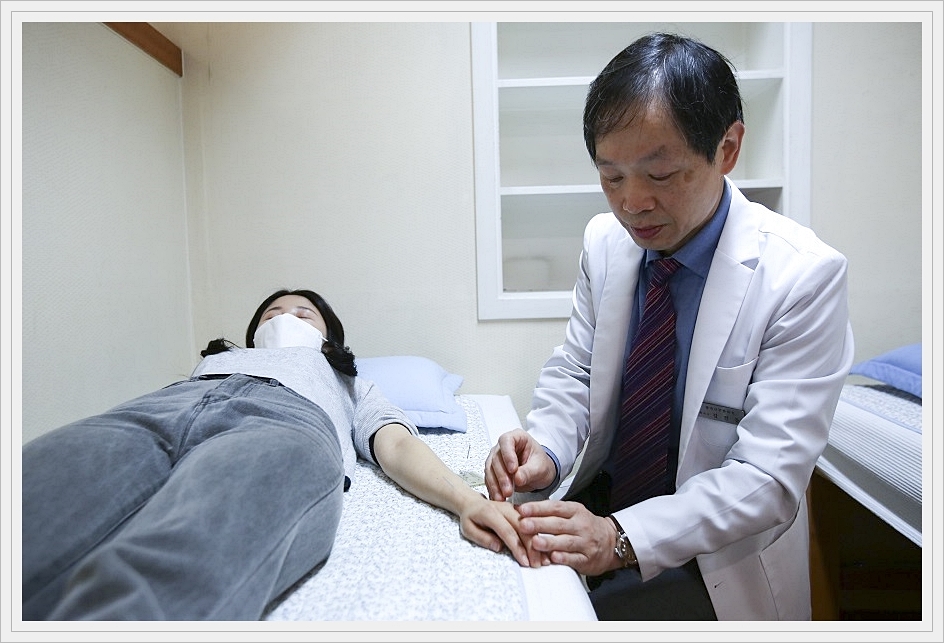 누워있는 환자의 손등에 침을 놓고 있는 한의사의 모습