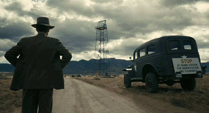 도로에 차가 서 있고 남자가 허리에 손을 올리고 풍경을 바라본다. 