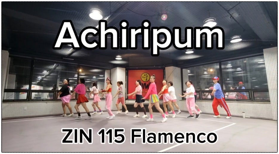 "ZIN 115 Flamenco 'Achiripum' 곡에 맞춰 단체로 줌바댄스를 추는 둔산줌바 회원들. 다양한 핑크 계열 의상을 입은 참가자들이 밝은 실내 체육관에서 신나고 활기차게 안무를 소화하고 있다. 중앙에는 ZUMBA 로고 배너가 배경으로 보인다