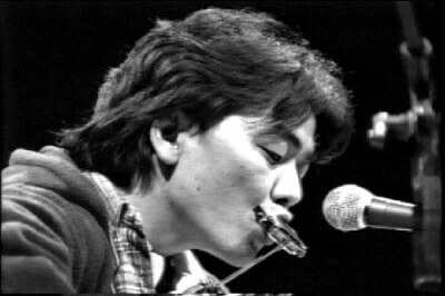 김광석이-목에-걸린-하모니카를-불고-있는-흑백-사진