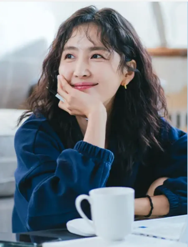 웰컴투삼달리-
곱슬머리를 한 삼달 큰언니가 왼속으로 턱을 괴고 미소를 지으며 뭔가 생각하는 이미지