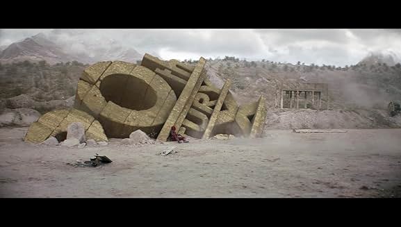 사막 한가운데 쓰러진 20th Century Fox 로고 앞에 앉아있는 데드풀의 장면