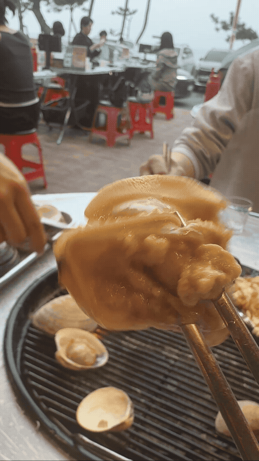 강릉 화니조개 야외 조개구이 테이블에서 큼직한 조개를 들어 올린 모습