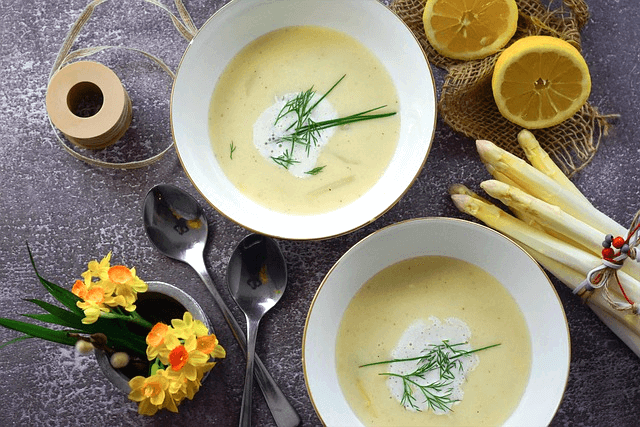 하얀 그릇에 희멀건 스프가 있다. 그릇이 2개다. 주변엔 숟가락 3개와 노란 꽃들이 있다.