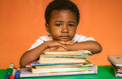 한 어린 아이가 책에 턱을 괴고 앉아 있는 모습