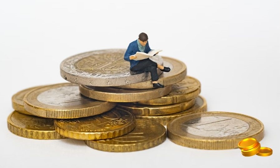 금융 공부의 중요성을 나타내는 이미지 - 금화 더미 위에 앉아 책을 읽고 있는 미니어처 사람 via unsplash