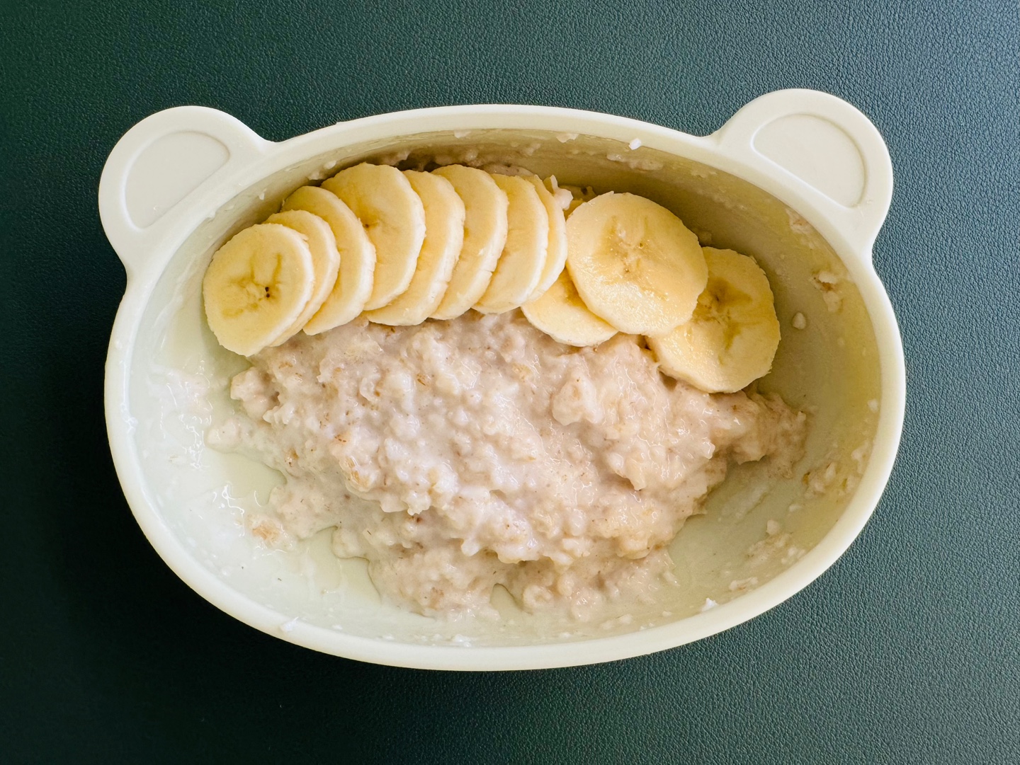 노란색 바나나 슬라이스가 얹어진 크리미한 오트밀포리지를 담은 아기 이유식 그릇