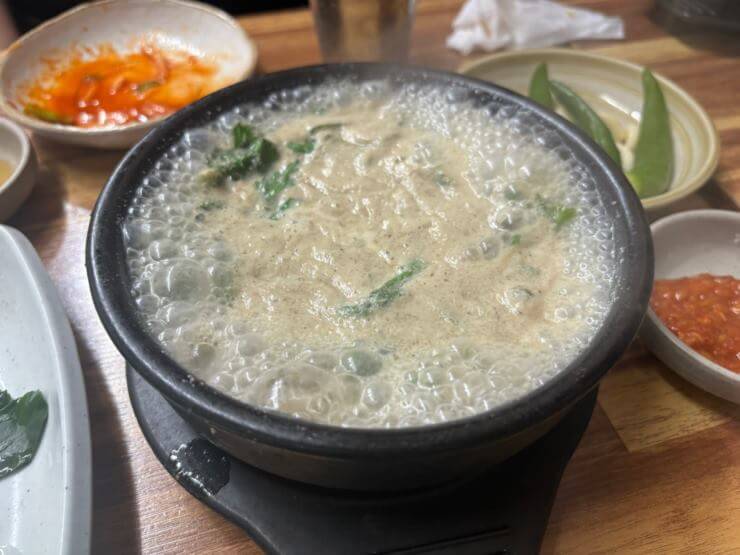 뚝배기가 끓고 있고, 뚝배기 안에 음식은 국물과 쑥이 있다.
국물은 갈색을 띄고 있고 국물 사이로 초록색 쑥이 보인다.