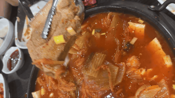 김치찜 안의 두툼한 고기 덩어리를 집게로 들어올리는 장면. 