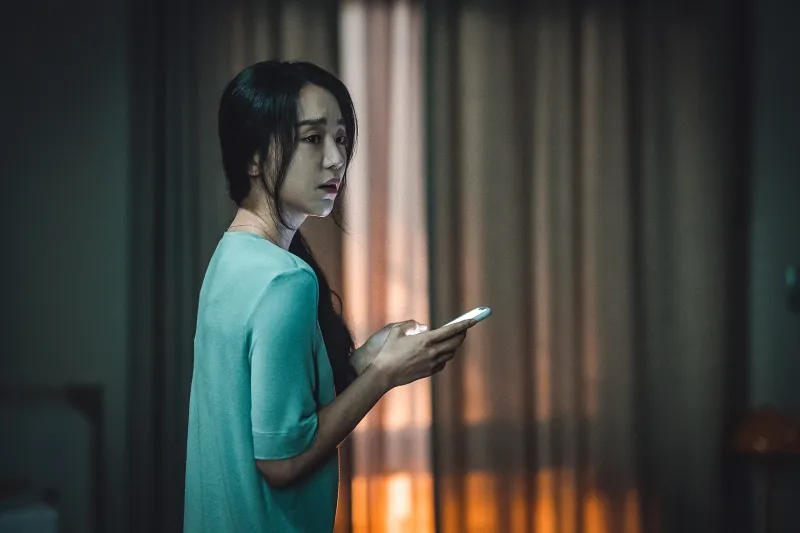 거실 커튼을 배경으로 어디를 바라 보며 한손에 핸드폰을 들고 있는 영화 타겟의 장수현