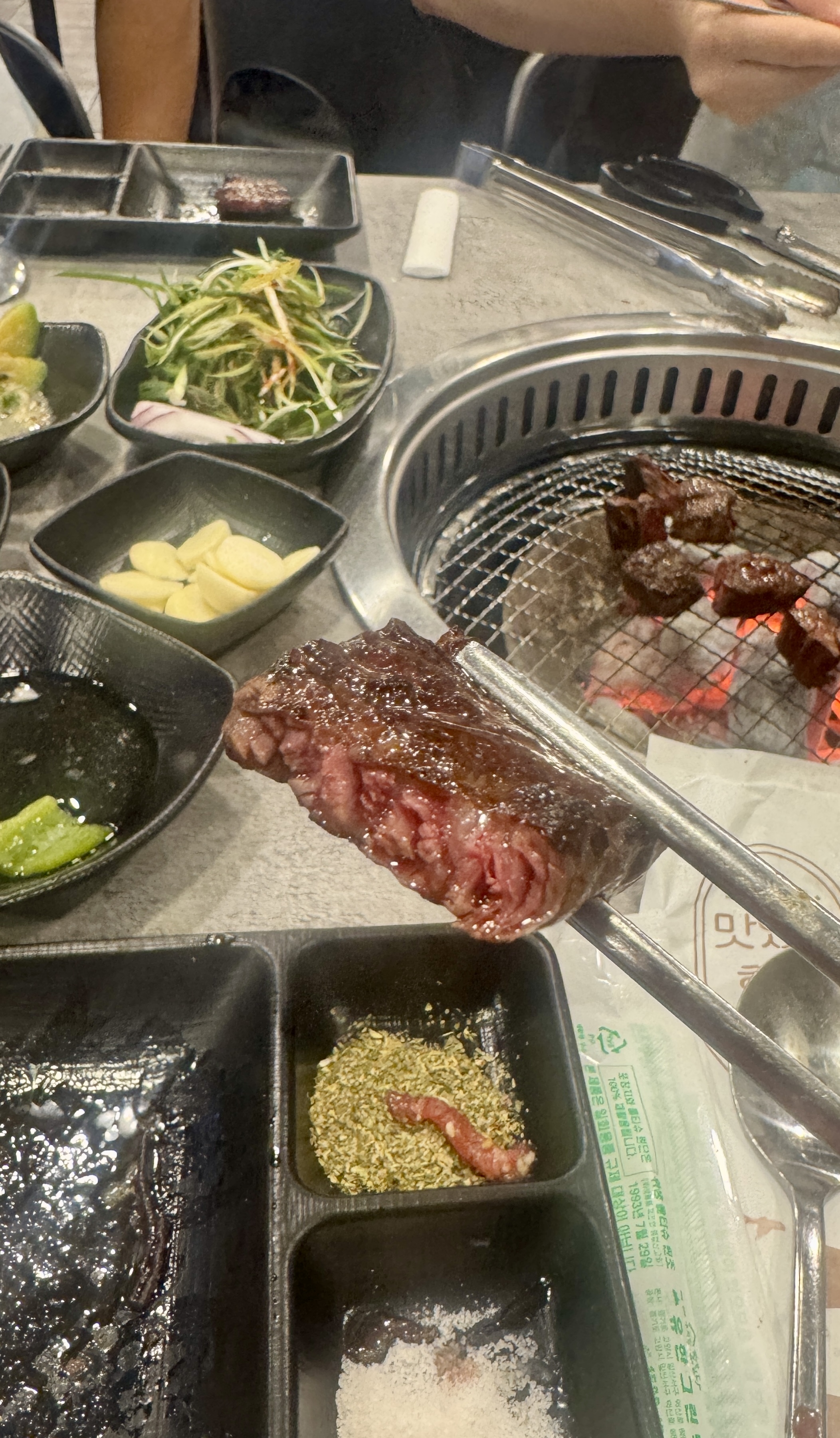 삼거리 명품한우에서 숯불 위에서 구운 한우 한 점을 젓가락으로 집은 모습. 겉은 잘 익고 속은 미디움 레어로 붉은 단면이 보인다.