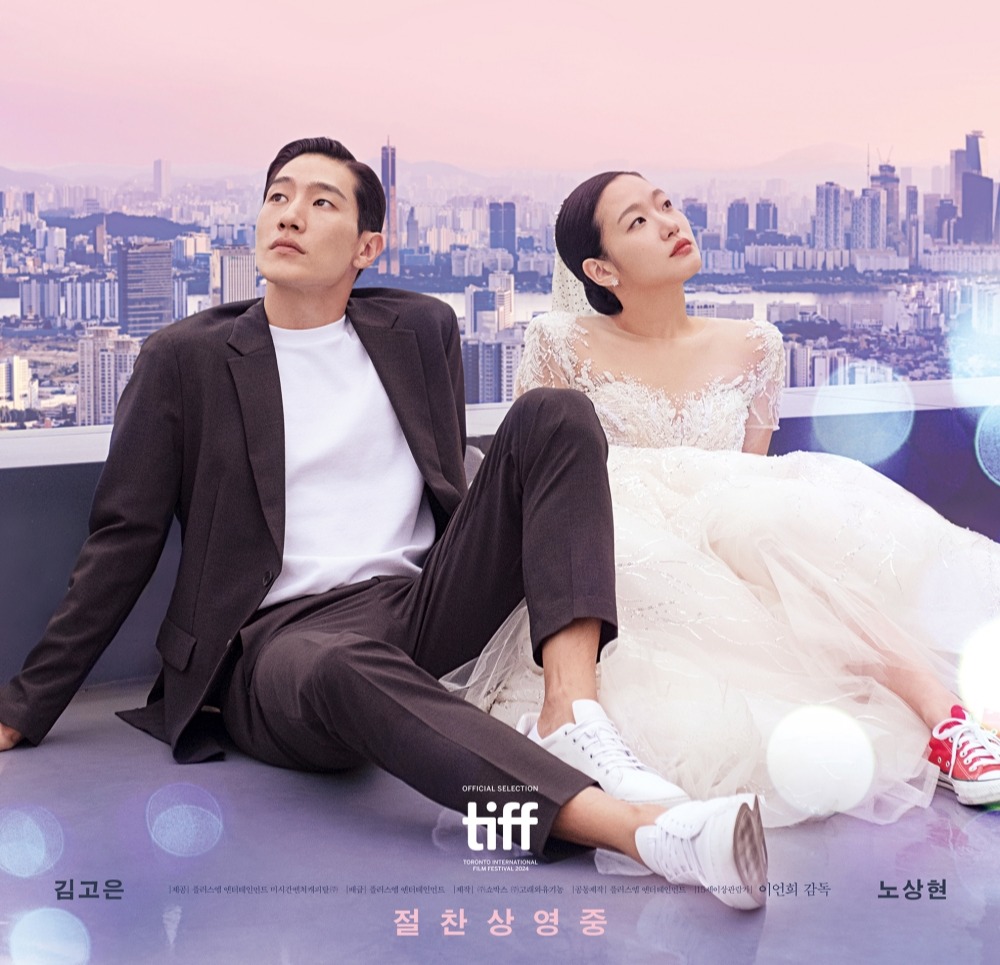 드라마 ‘대도시의 사랑법’ 공식 포스터, 정장을 입은 남자 주인공과 웨딩드레스를 입은 여자 주인공이 도시의 스카이라인을 배경으로 나란히 앉아있는 모습. 핑크색 계열의 따뜻한 분위기와 함께 도심의 감성을 표현한 이미지.