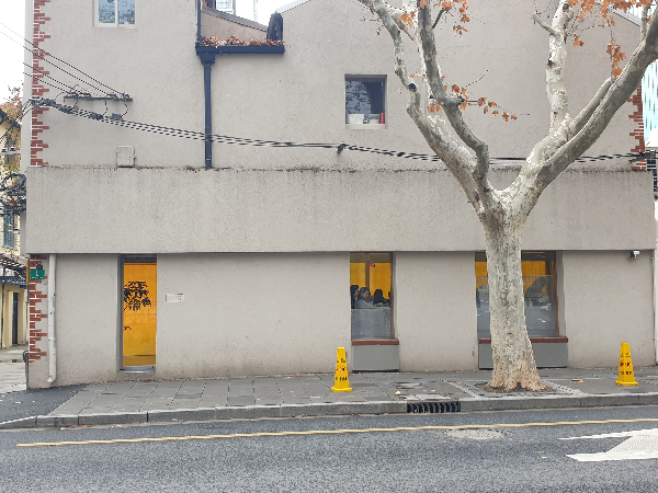 회색 건물 1층 유리문 하나와 2개의 창에서 노란 불빛이 흘러 나온다.